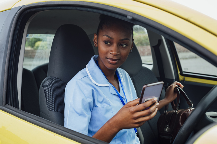Nurse arriving at a patient's home in the North East of England. She is sitting in her car using her mobile phone.