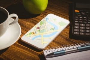 cup of coffee calculator apple pen and journal on desk next to phone with a map 