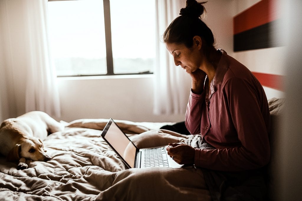 Sick woman making an appointment with doctor via internet with her dog on bed