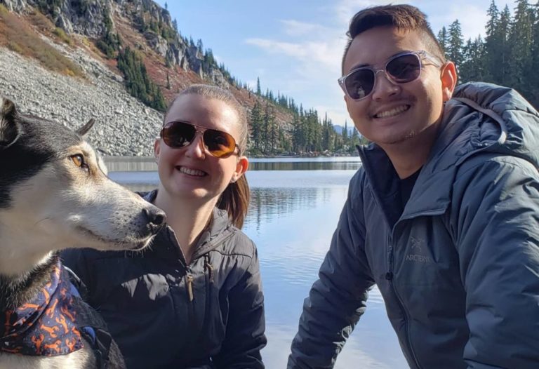 TNAA and TotalMed allied traveler couple hang out with their dog in front of a beautiful lake and a mountain view.