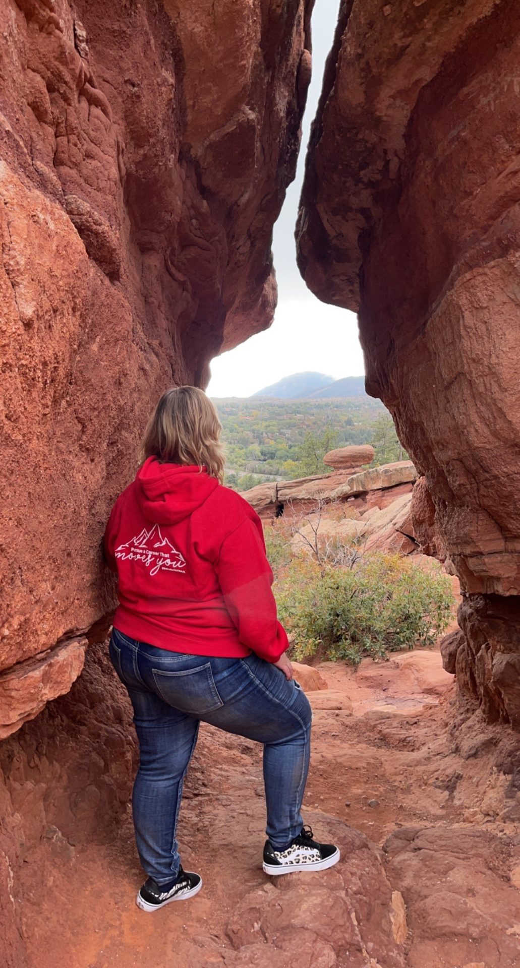blonde woman in red hoodie looks at a rocky landscape