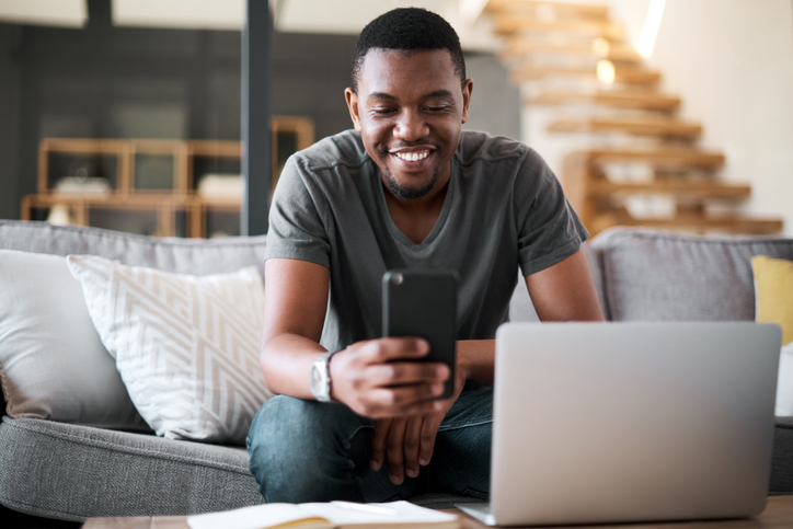 Shot of a young man using a cellphone and laptop at home