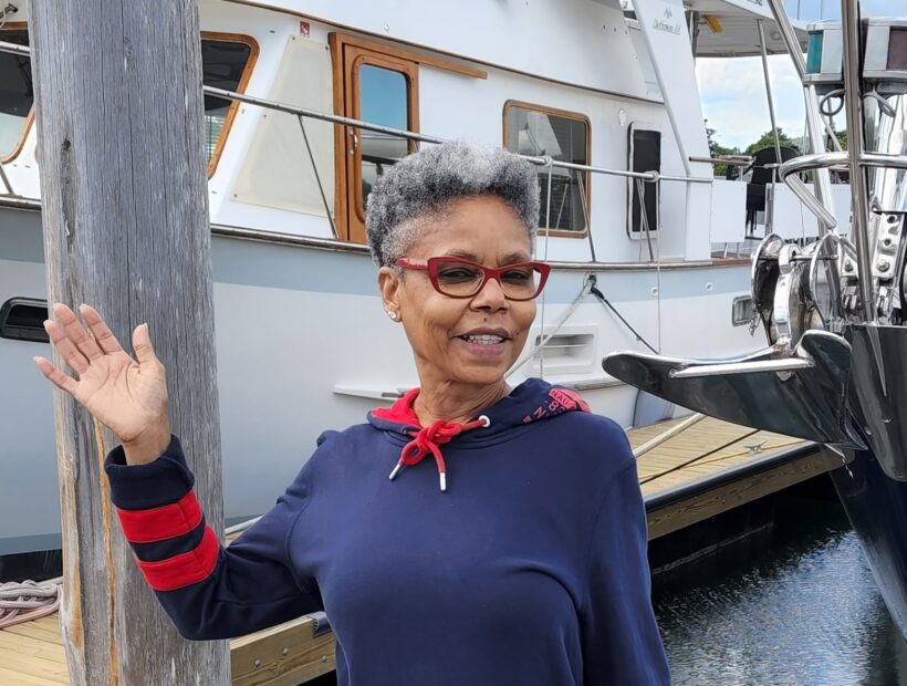 Debbie, a travel nurse, waving while standing in front of a boat