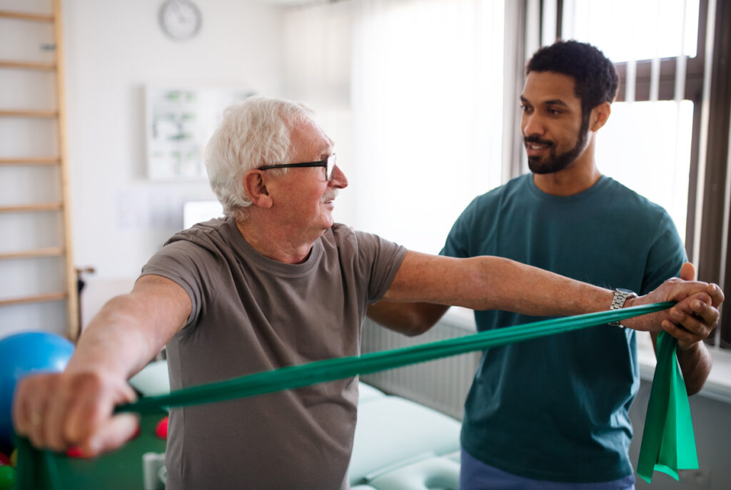 Young physiotherapist exercising with senior patient in a physic room