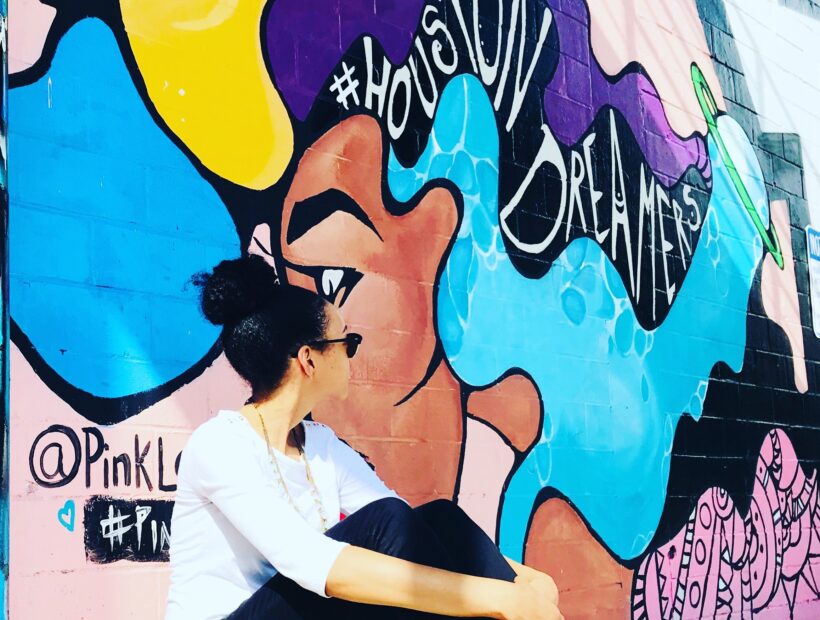 TNAA employee looking off camera while sitting next to a Houston mural