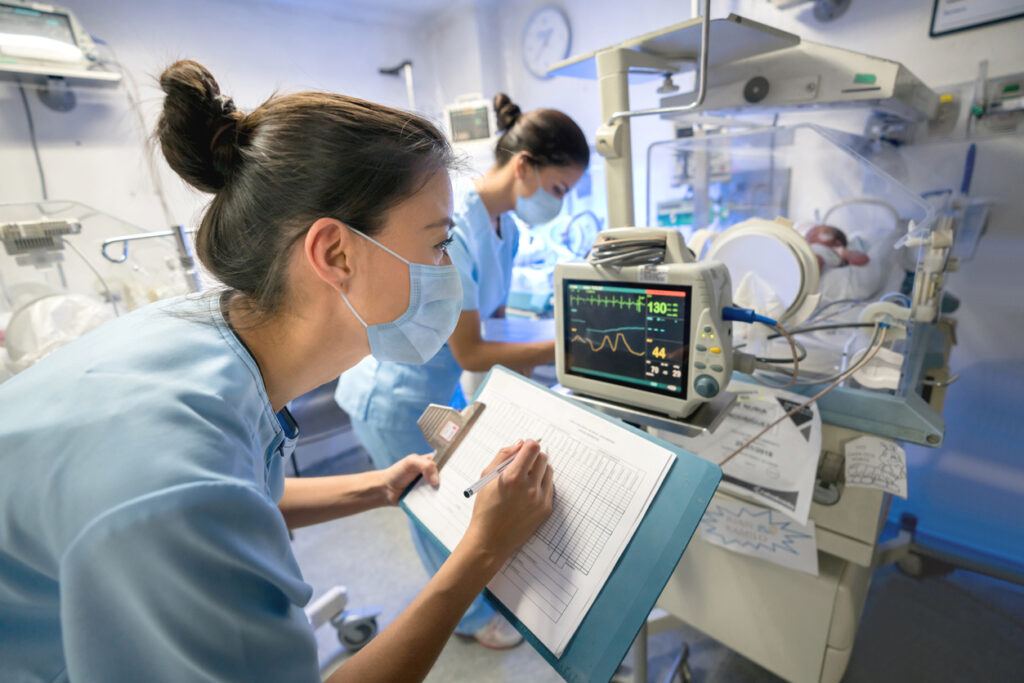 Nurse monitoring a premature newborn in an incubator while wearing a facemask