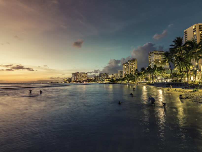 Night panorama of Waikiki Beach and building by the shore line with palm trees in Honolulu