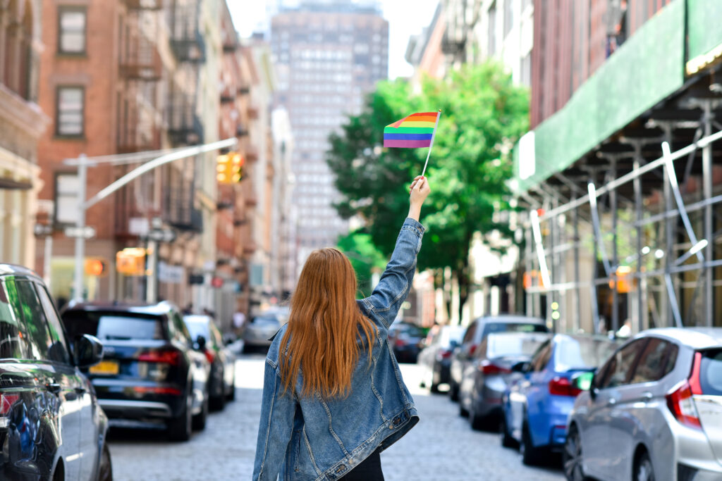 Woman holding a rainbow Pride flag in New York City, showing LGBTQ+ pride and visibility in an urban setting.
