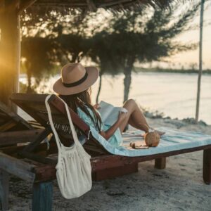 Woman reading a book while lounging on a sandy beach.